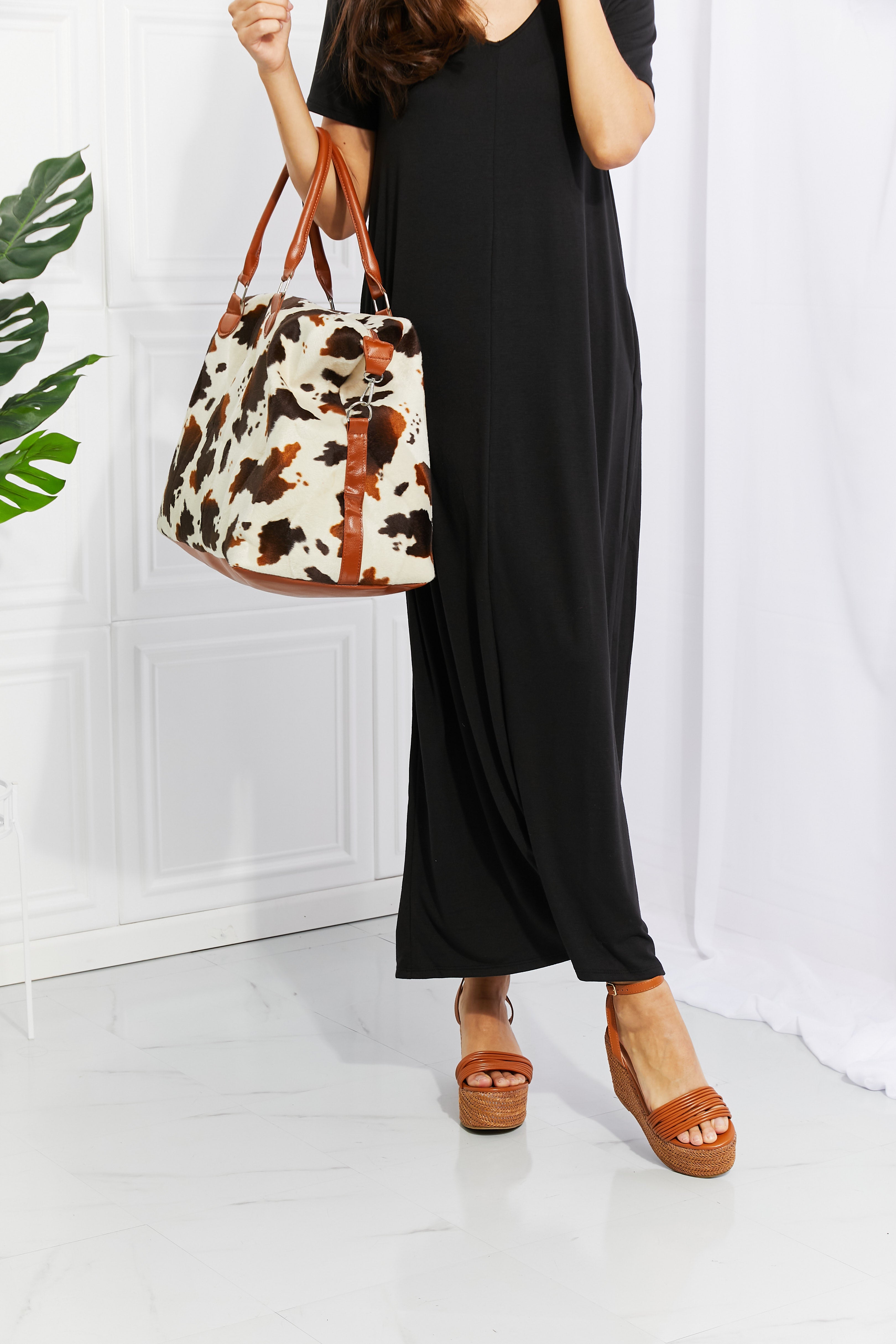 Cow print plush weekender bag with tan handles and zip-top tote shape