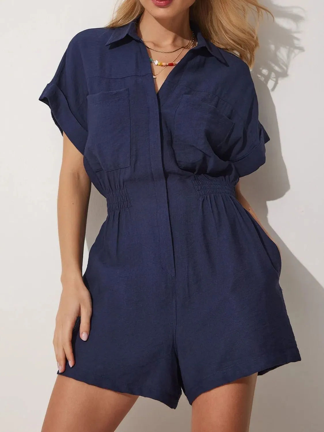 Dark blue short-sleeve romper with collar, button front, patch pockets, and gathered waist.