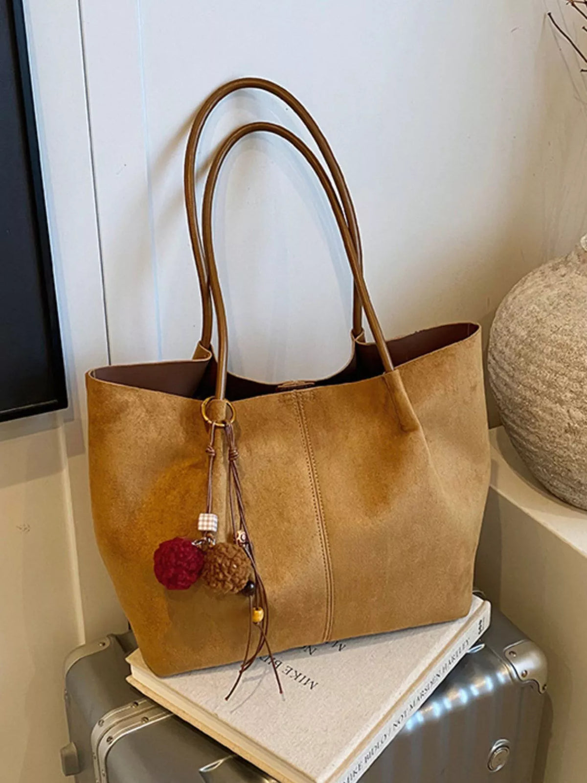 Tan suede large tote bag with long handles, center seam, and pom-pom keychain.