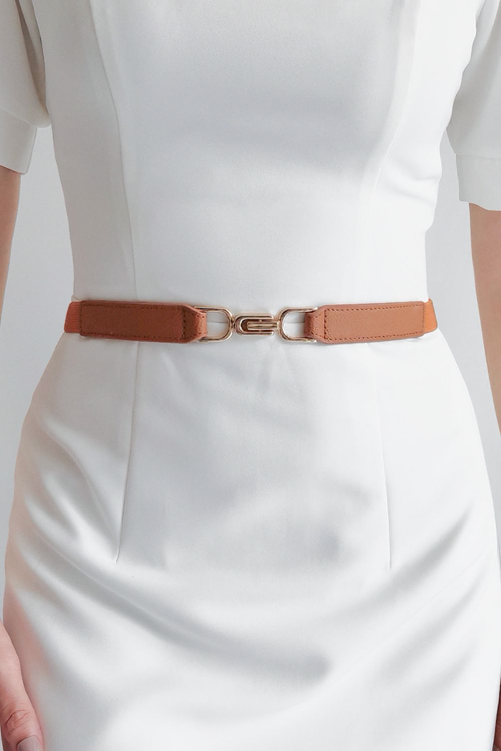 Caramel elastic buckle belt worn over a white dress, silver-tone hardware
