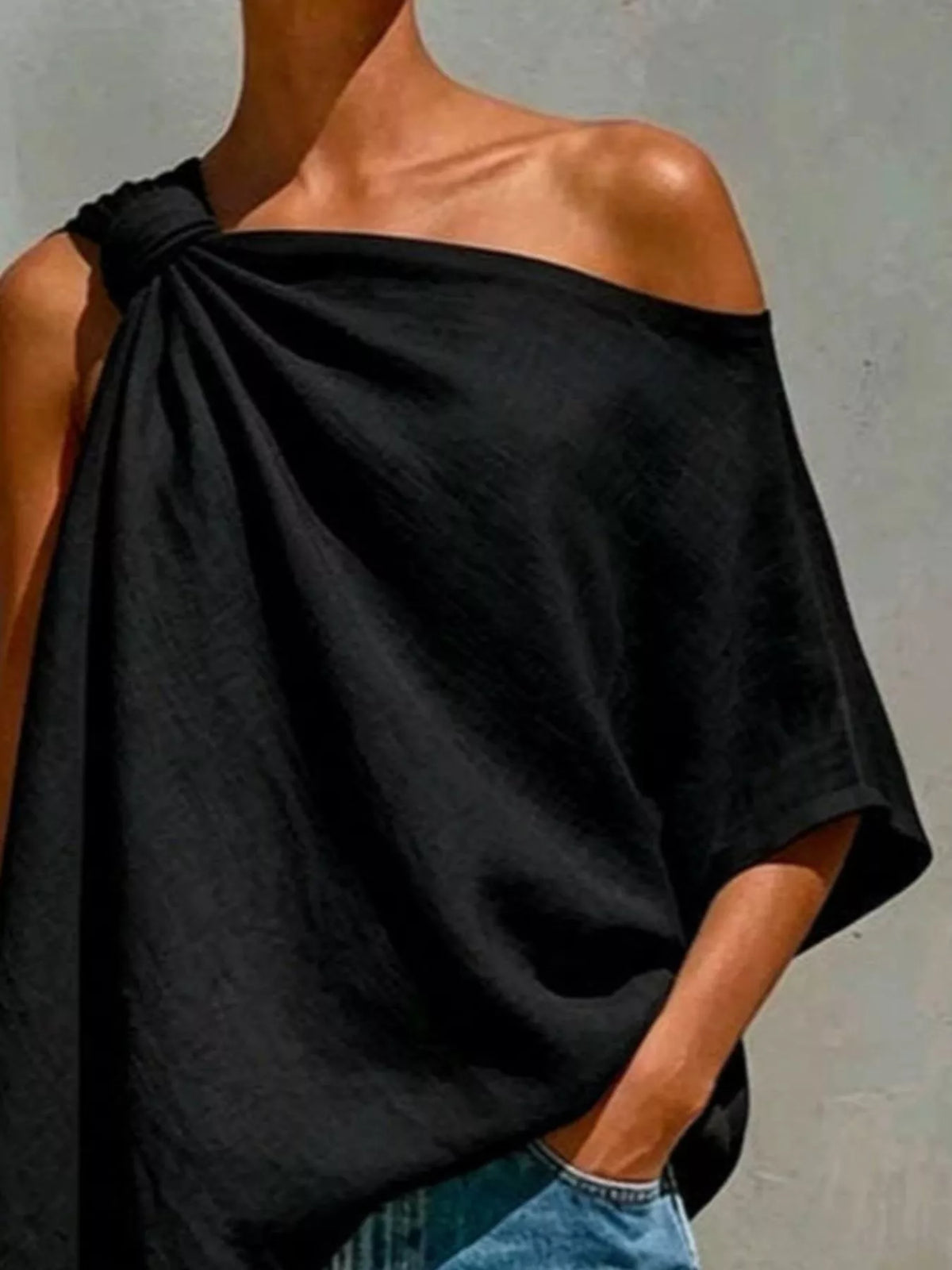 Black one-shoulder blouse with knotted shoulder detail and loose draped silhouette