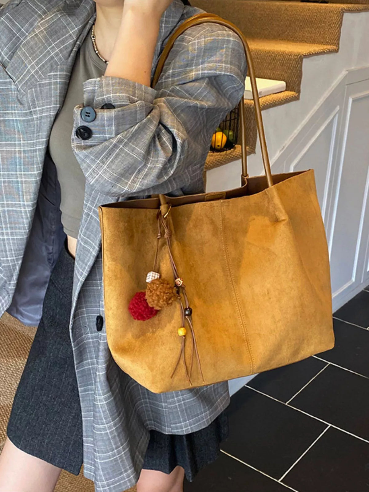 Tan suede tote bag with long handles, front zip pocket, and pom-pom charm.