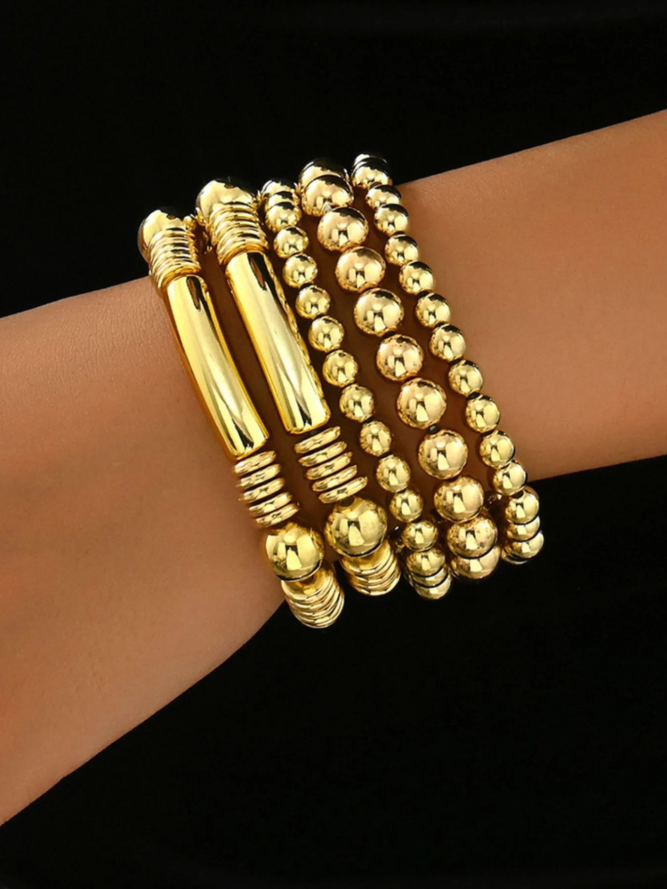 Gold beaded bracelet set with three shiny stacked strands and tube charm