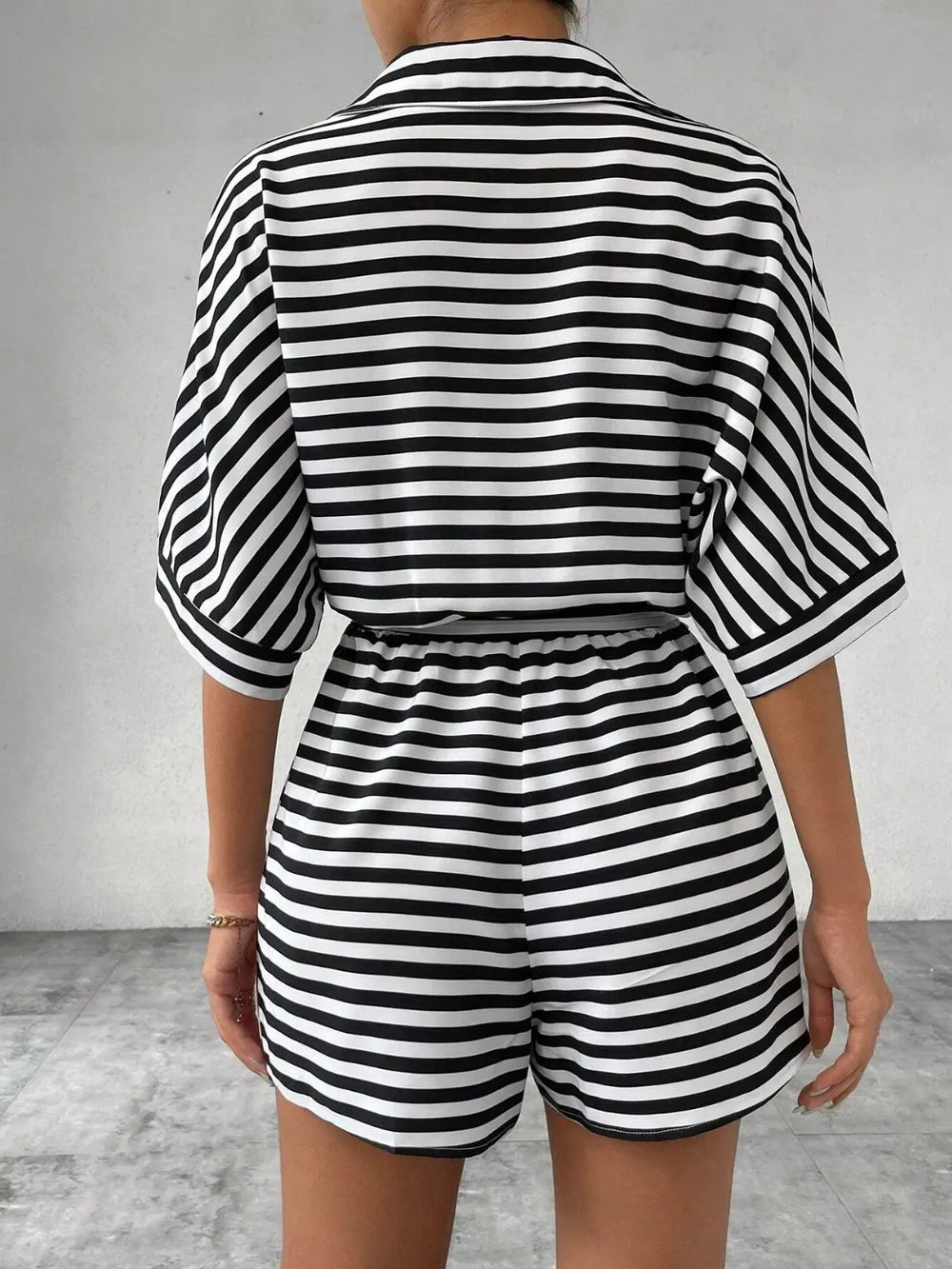 Back view of black and white striped button-front romper with tie waist and cuffed sleeves