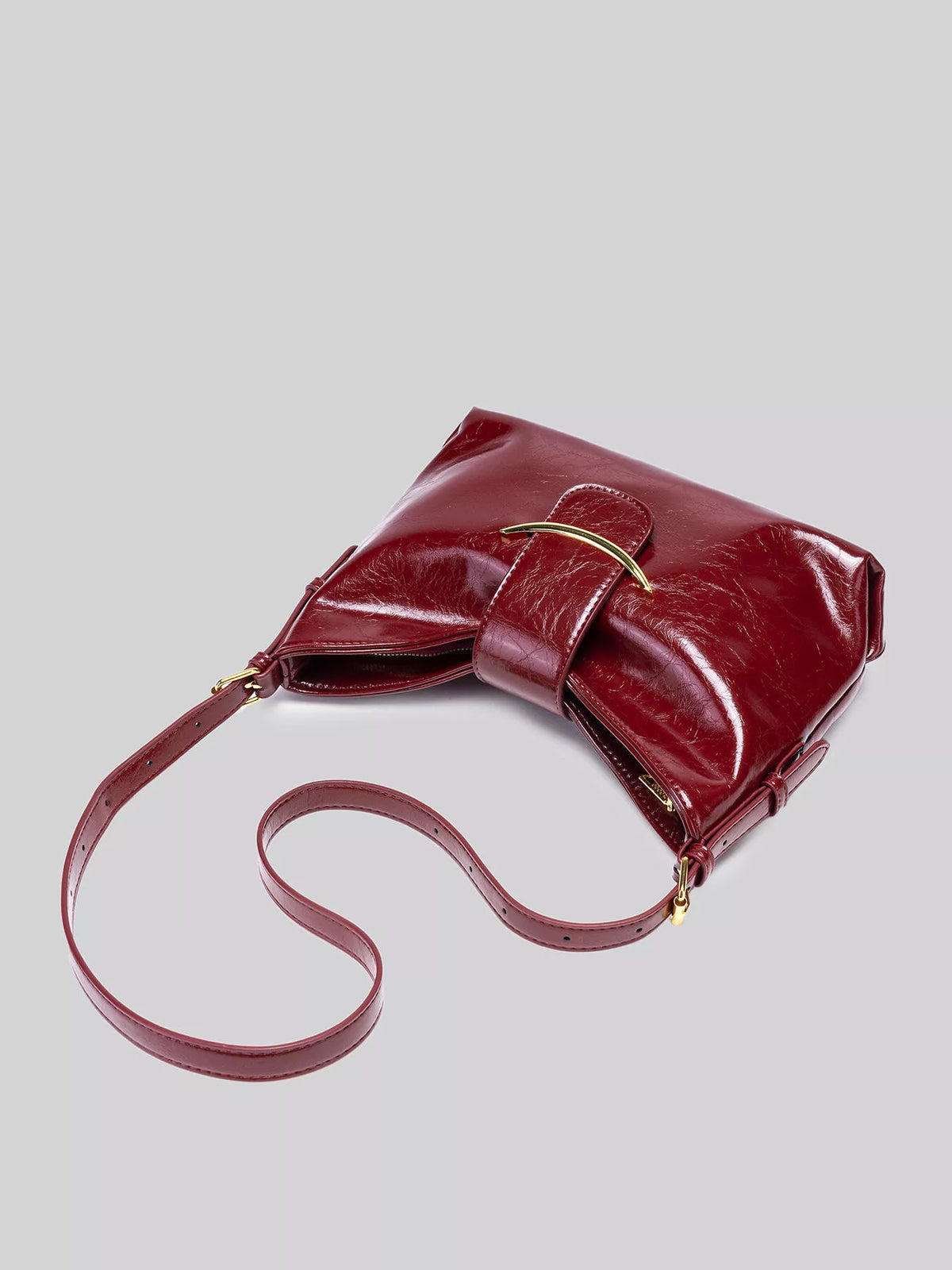Wine red gloss vegan leather crescent shoulder bag laid on side with shoulder strap