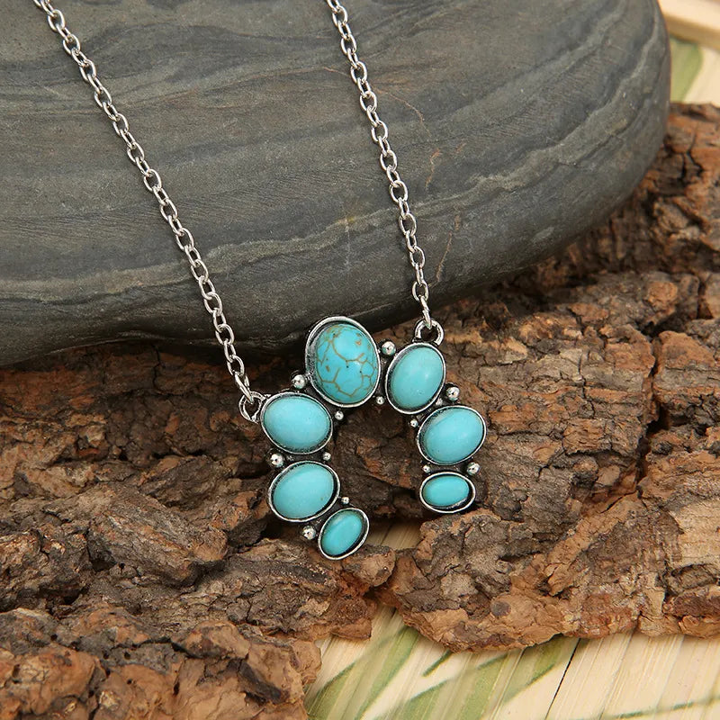 Turquoise oval stone pendant necklace on silver-tone chain, clustered flower design.