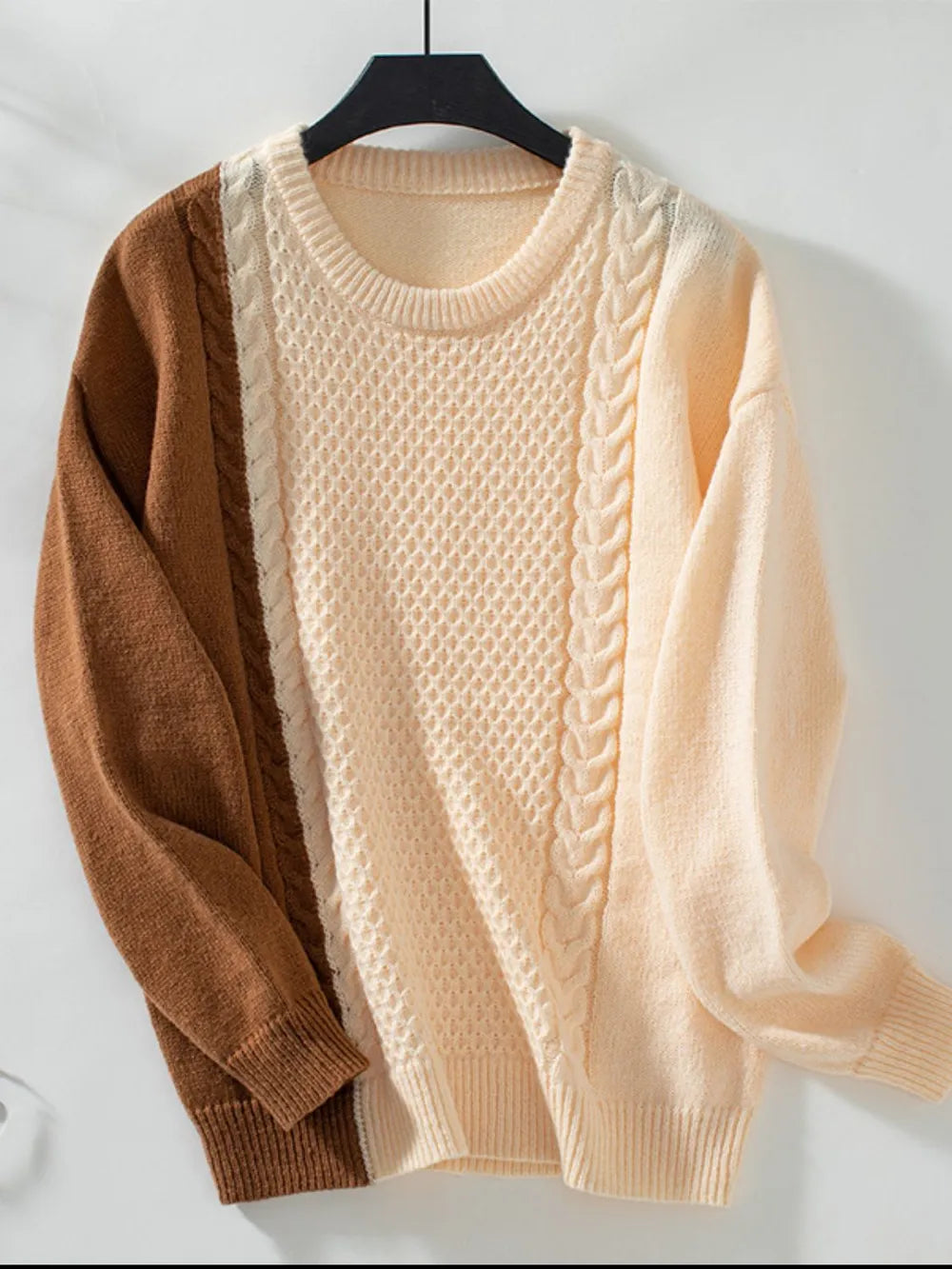Two-tone cable knit sweater with cream body and caramel sleeves on a hanger
