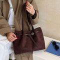 Dark brown suede shoulder bag with top handles, front pocket, and adjustable strap