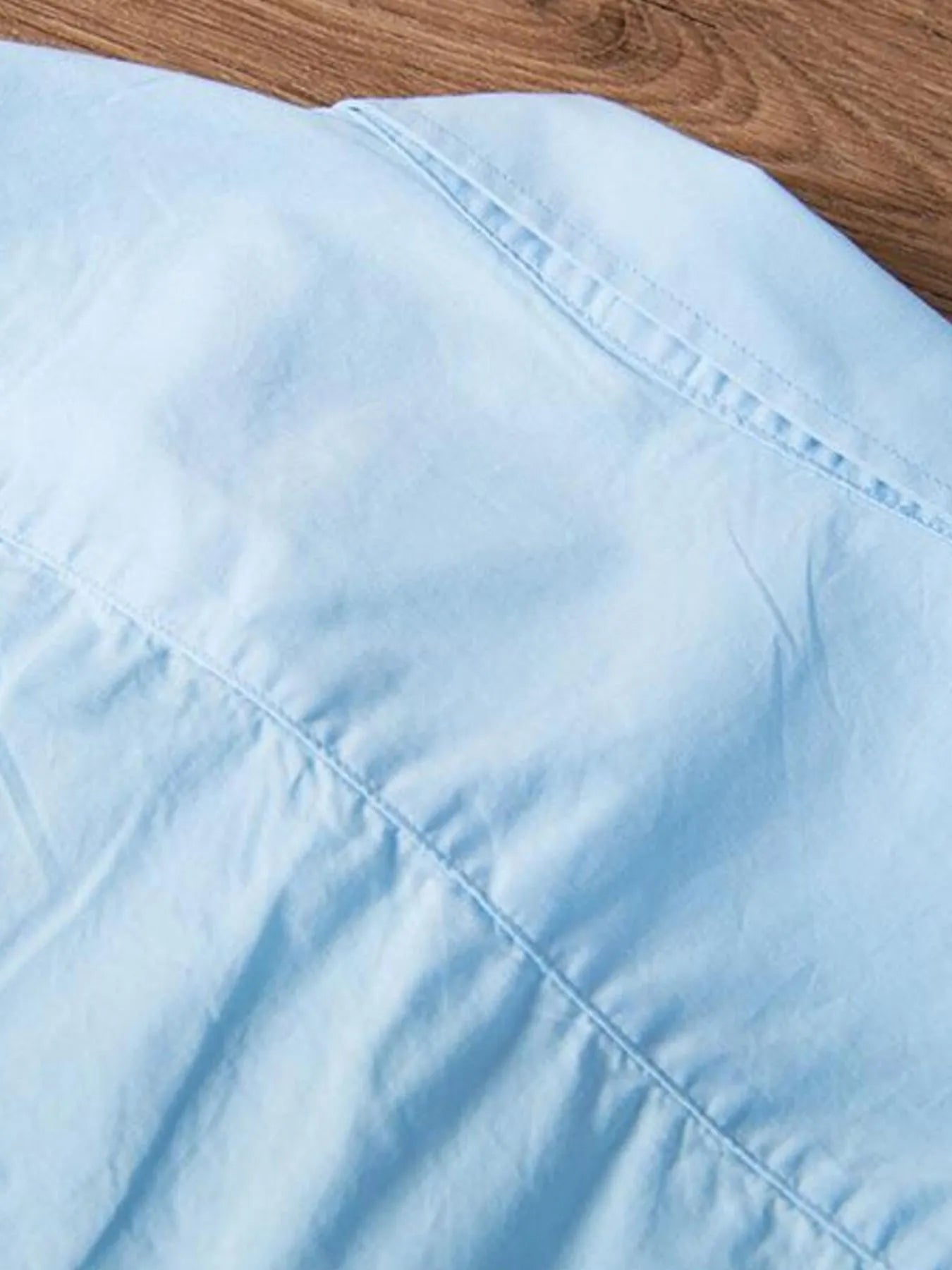 Close-up of light blue button-up shirt with diagonal seam detail and stitching