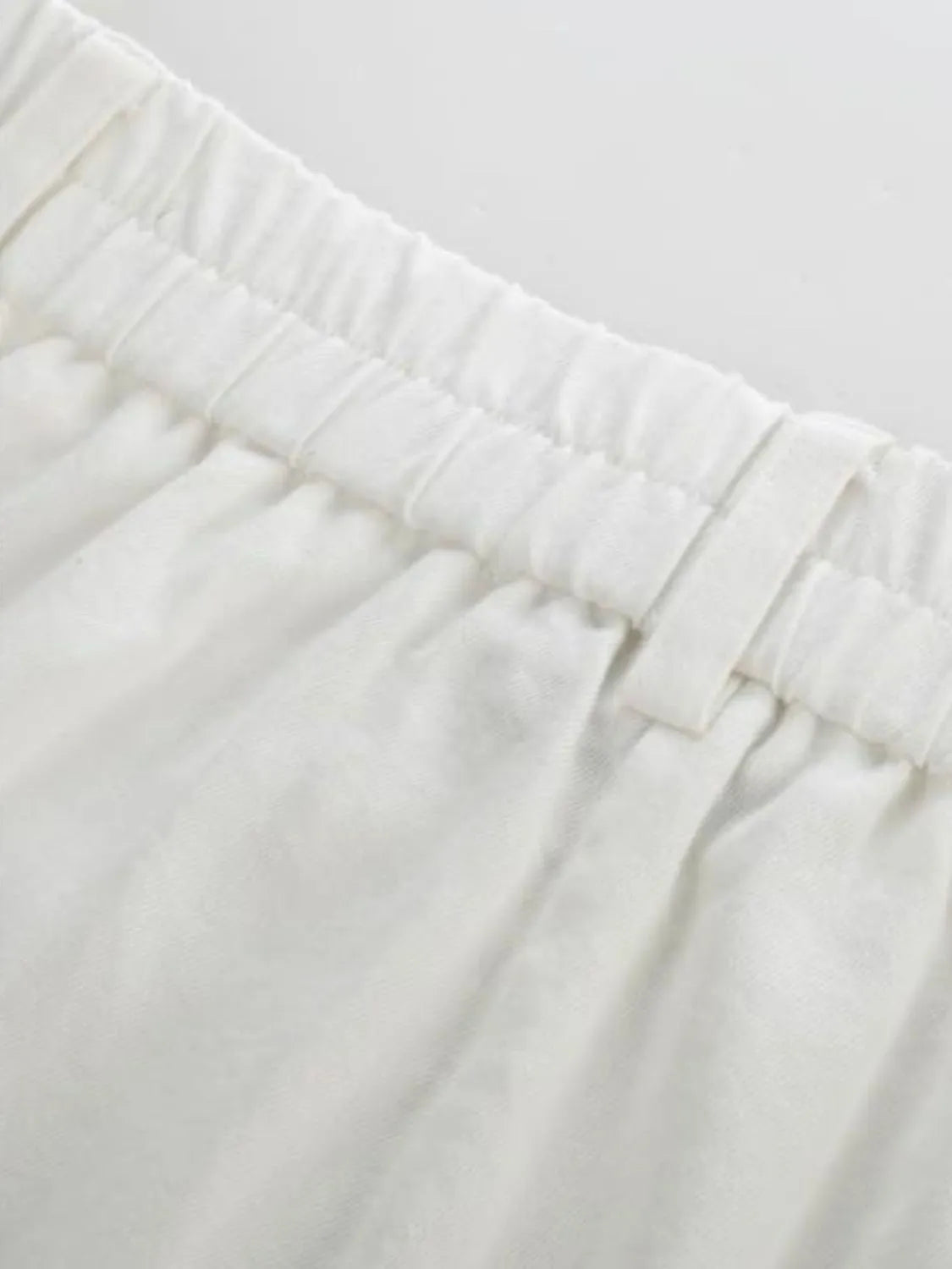White high-waist pants close-up of elastic waistband and stitched front seams