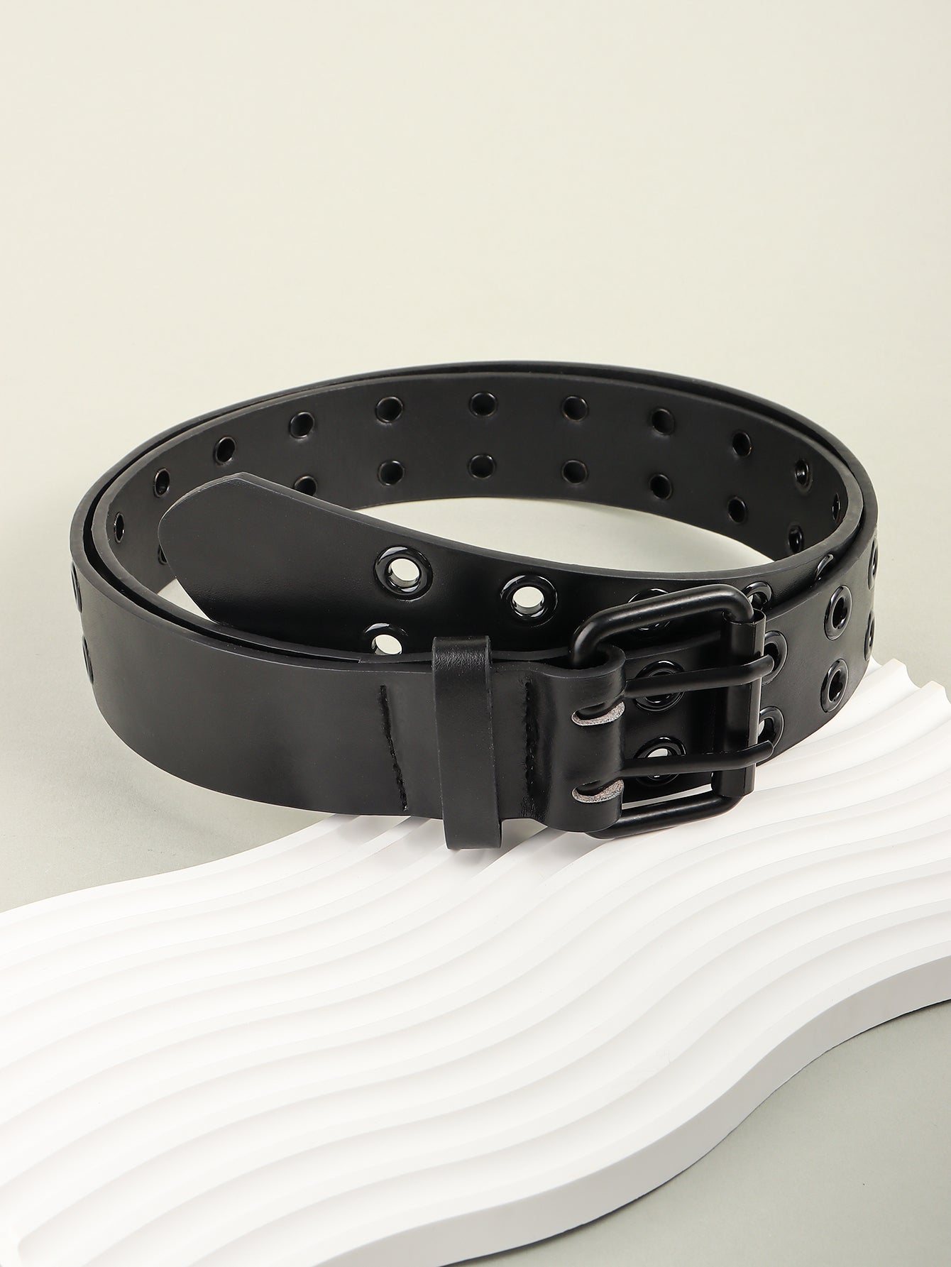 Black grommet belt with square buckle and eyelet holes, styled on folded base.