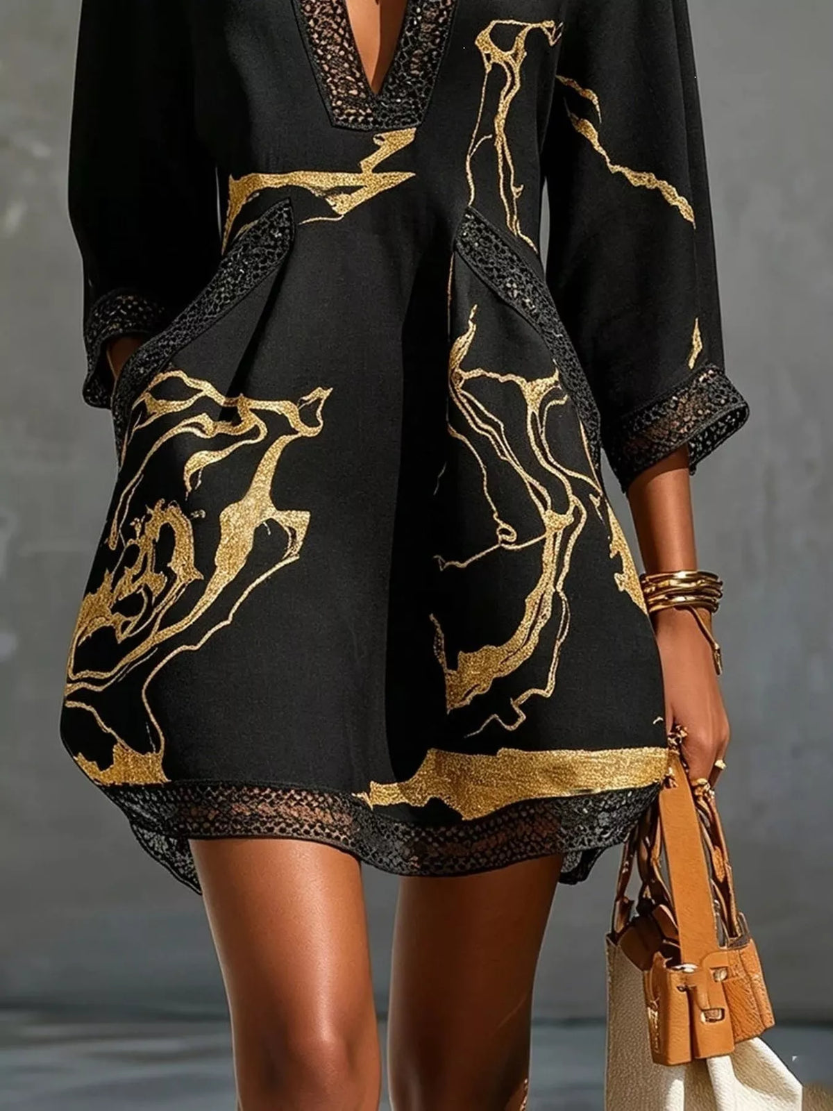 Black mini dress with gold abstract print and lace-trim hem, standing front view