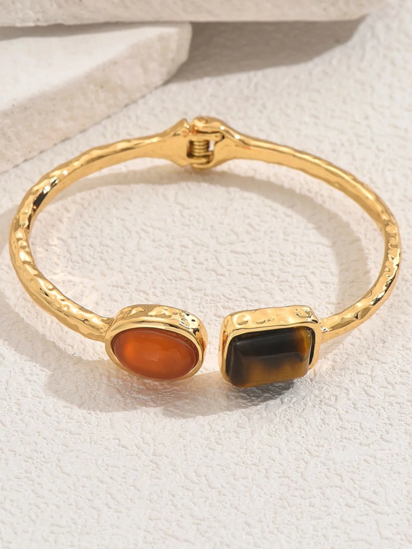 Gold tone open cuff bracelet with orange oval and dark square geometric charms