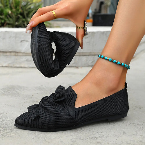 Black point-toe slip-on flats with bow detail at the toe and low sole