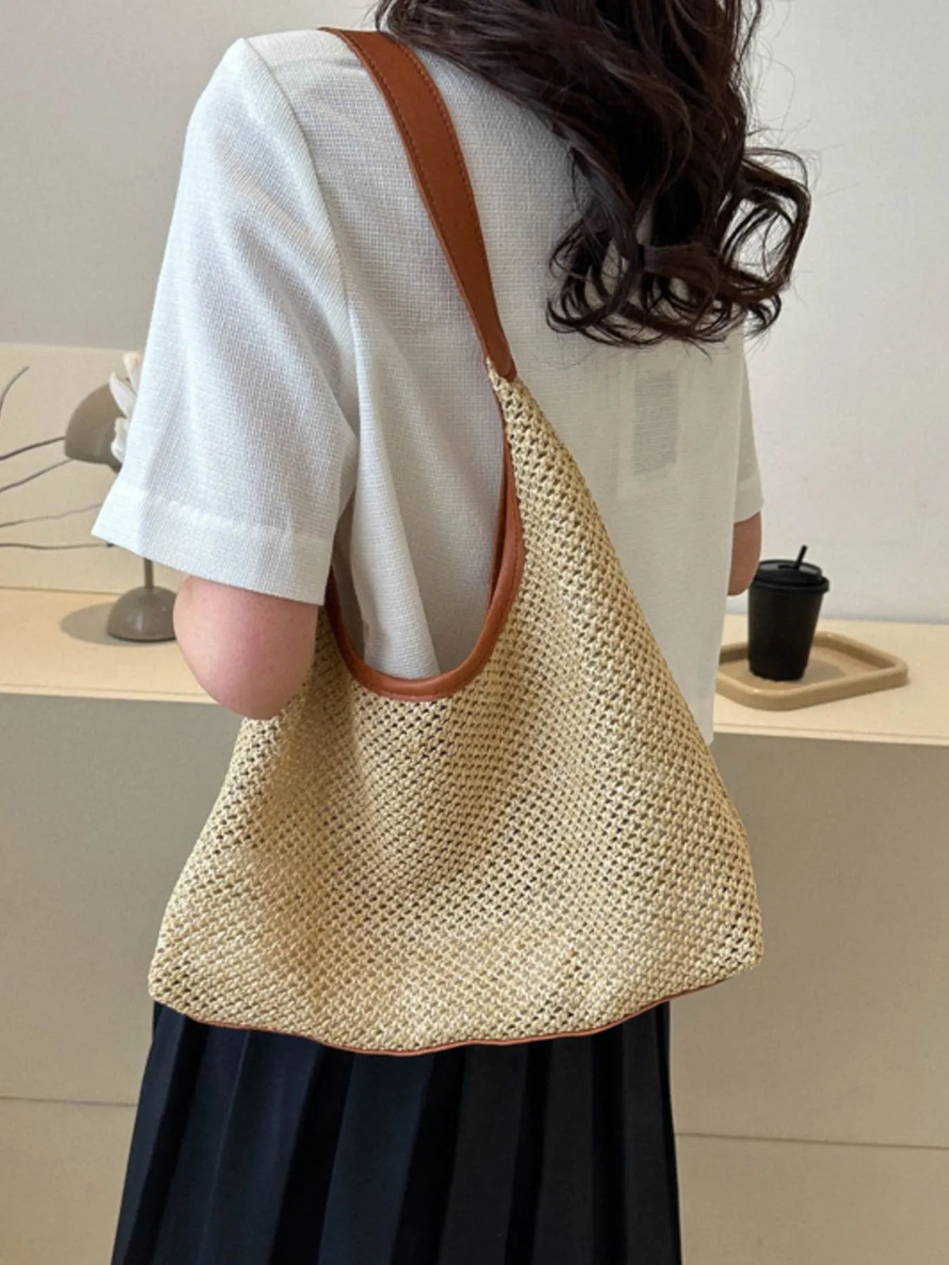 Woven straw shoulder bag in tan with brown handles, worn over shoulder