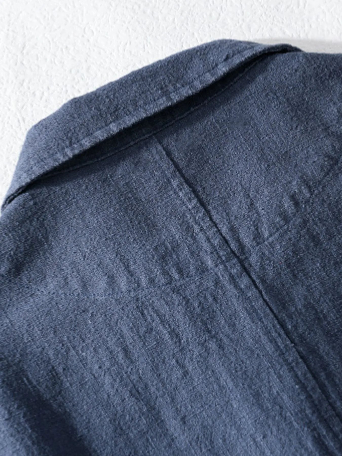 Dark blue button-up shirt shoulder and yoke with textured fabric and folded seam.