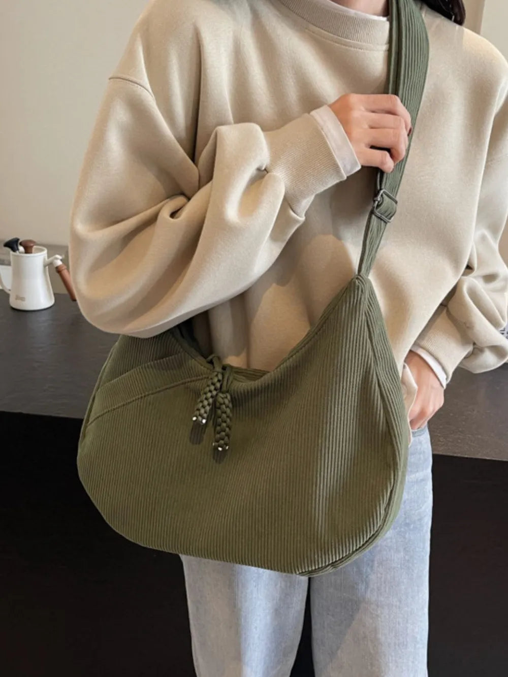 Moss green ribbed shoulder bag on model with adjustable strap and braided tassel pull