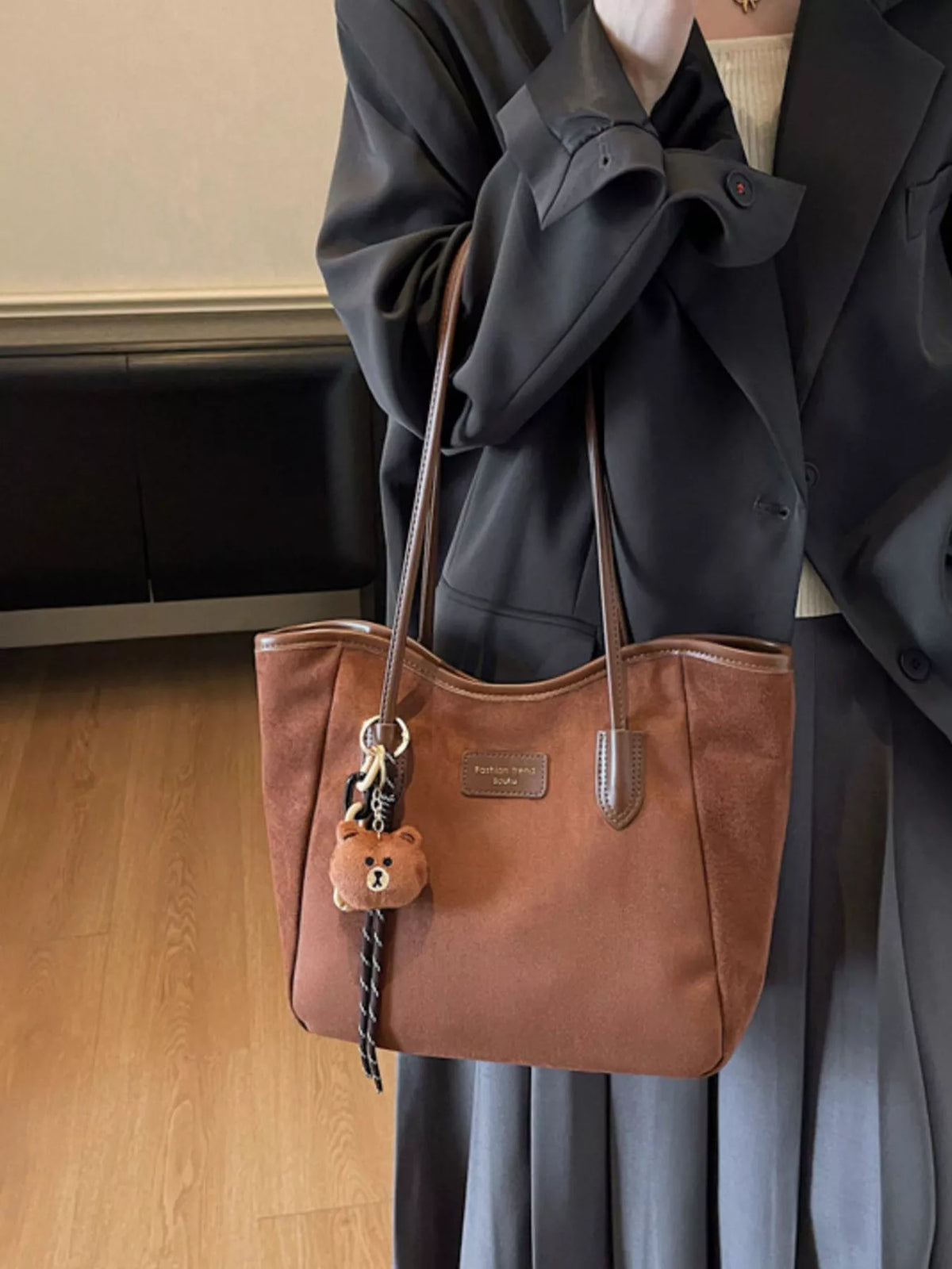Brown suede tote bag with long handles, zipper top, and bear keychain tassel