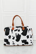 Cow print plush weekender bag with tan handles and structured zip-top shape