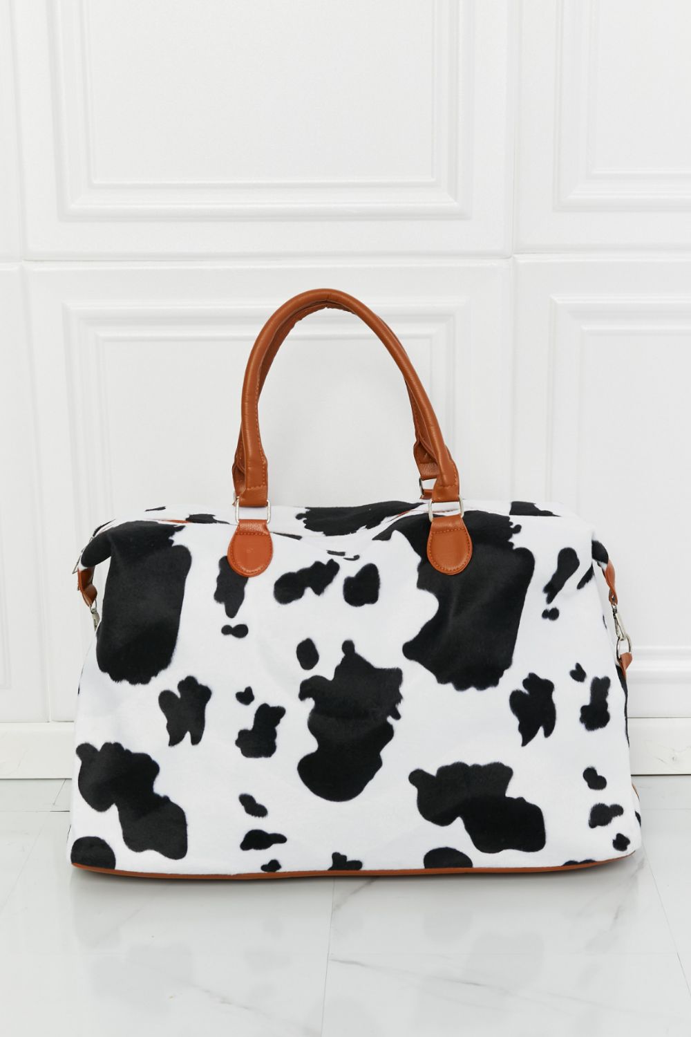 Cow print plush weekender bag with tan handles and structured zip-top shape