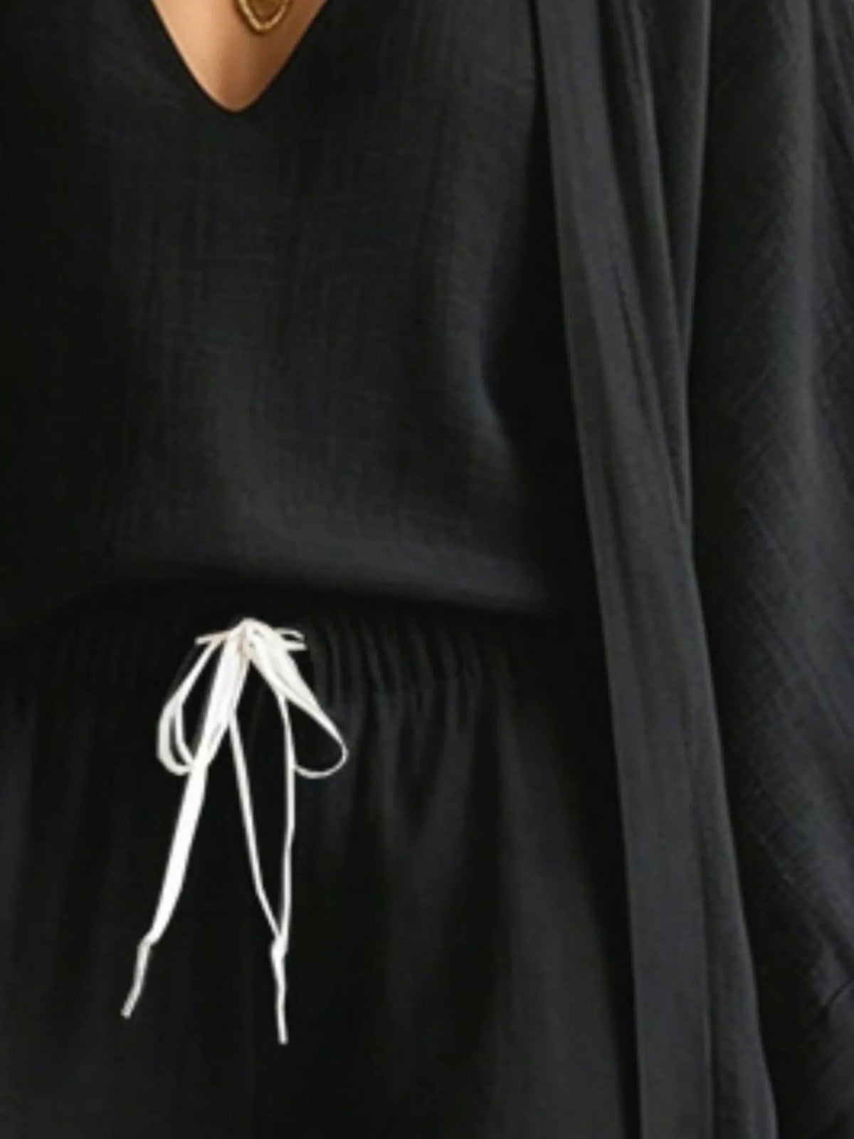 Black drawstring waist pants detail with open cardigan overlay, close-up crop