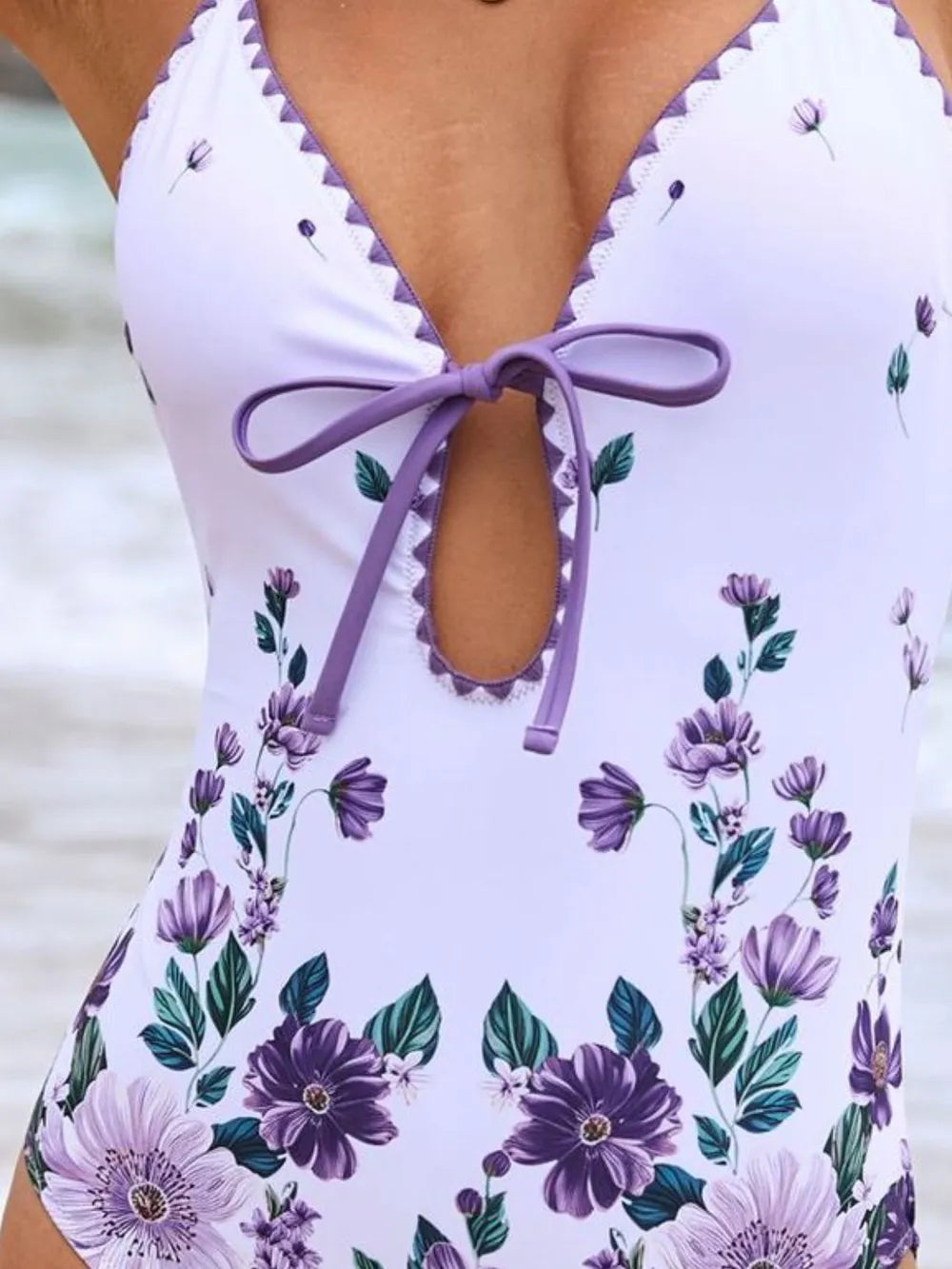 Close-up of white floral one-piece neckline with scalloped trim and purple tie bow