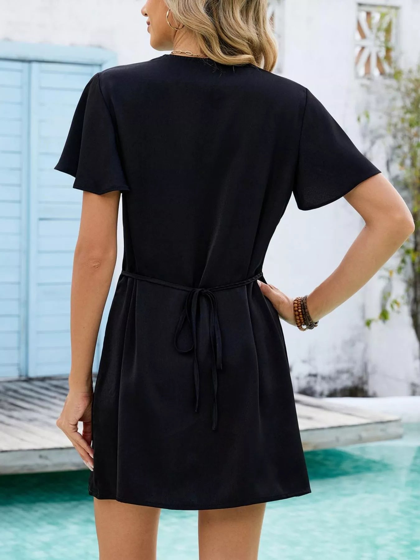 Cedar & Moore Notched Flutter Sleeve Mini Dress in black with waist tie, back view.