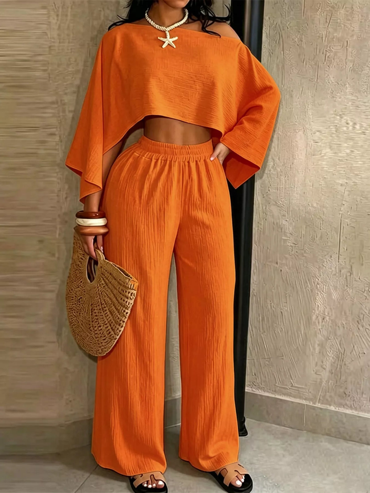 Orange wide-leg pants set with boat-neck crop top and draped sleeves.