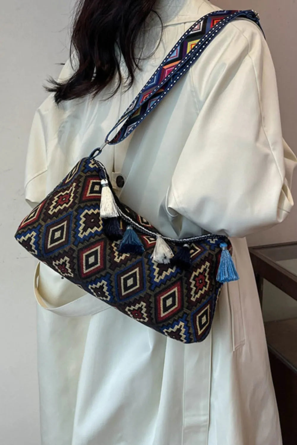 Geometric shoulder bag with adjustable strap and tassel fringe, worn with a cream dress