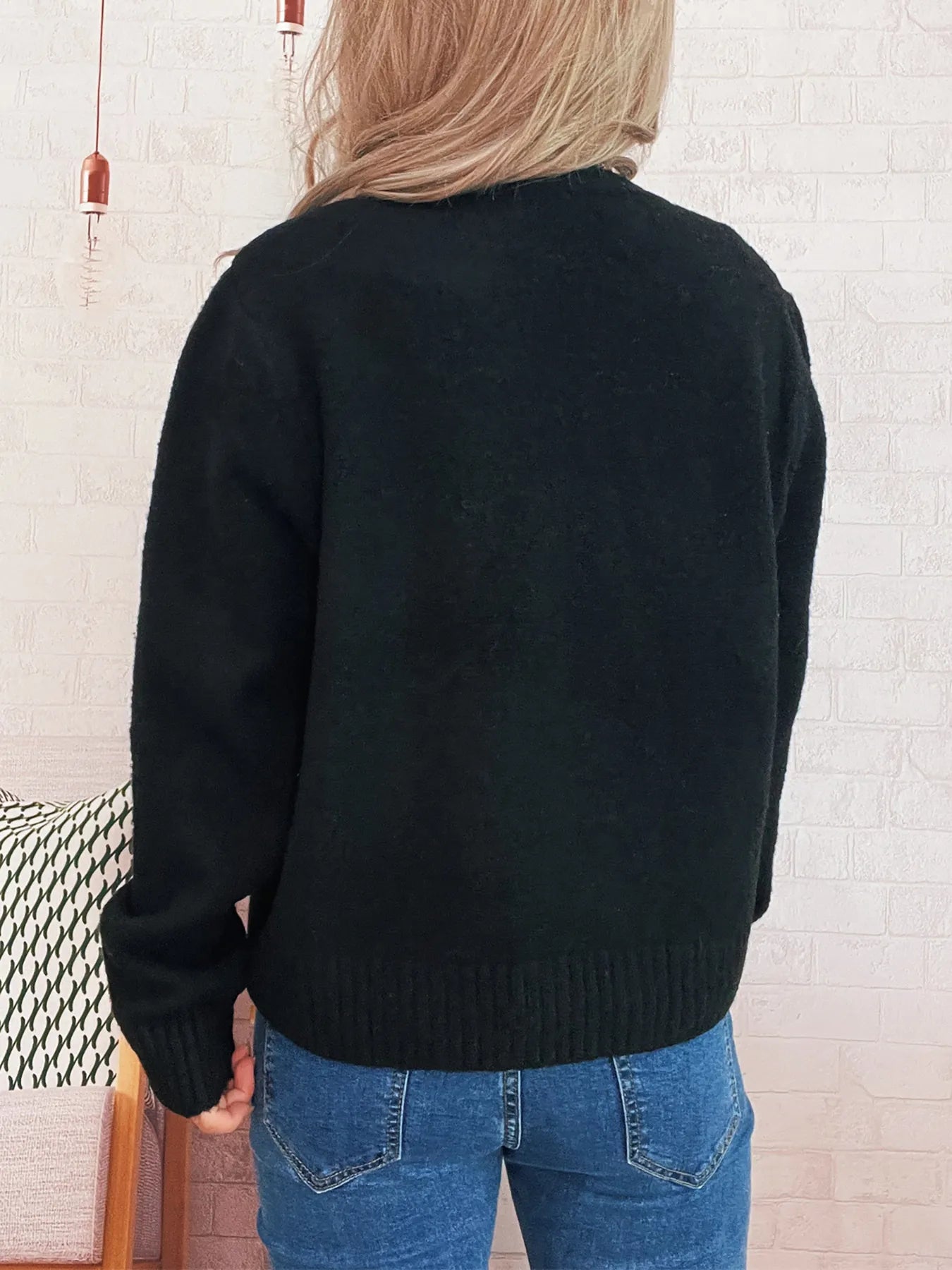 Black cardigan back view with ribbed hem and long sleeves, knit texture.