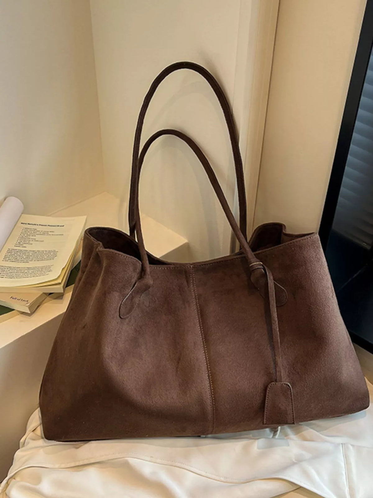 Brown suede tote bag with dual handles, side eyelet loops, and front strap pocket