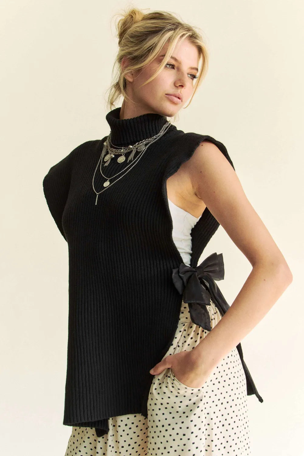 Black sleeveless rib knit turtleneck top with front bow at side slit