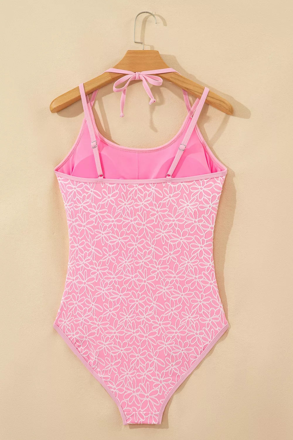 Blush pink floral halter one-piece swimsuit on wooden hanger, tie-back straps