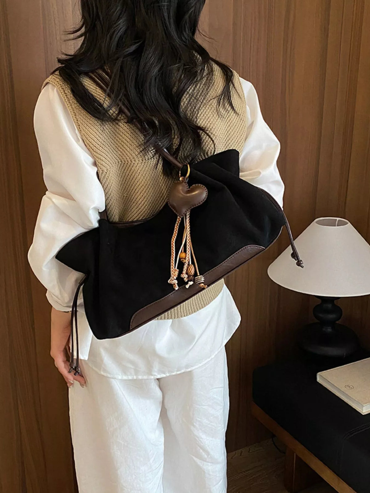 Black suede drawstring shoulder bag on shoulder with heart charm center and tassel ends