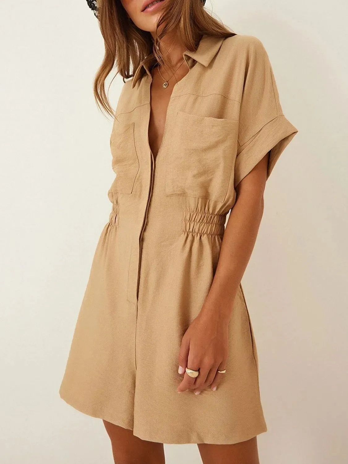 Tan short-sleeve romper with collar, button front, patch pockets, and elastic waist detail.