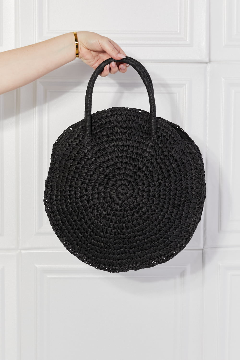 Black round woven straw rattan handbag with two short top handles, held up