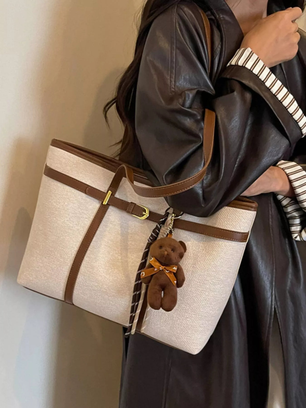 Off-white tote bag with brown stripe bands, buckle detail, and teddy keychain