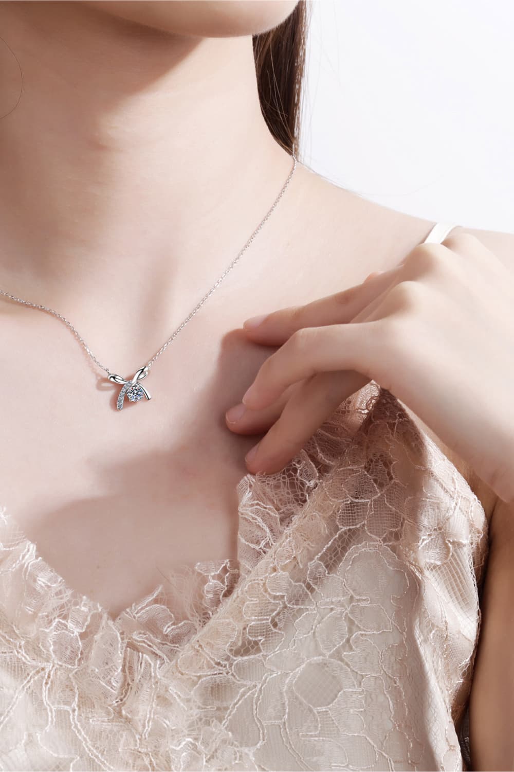 Moissanite sterling silver necklace worn with bow pendant and round center gemstone, close-up