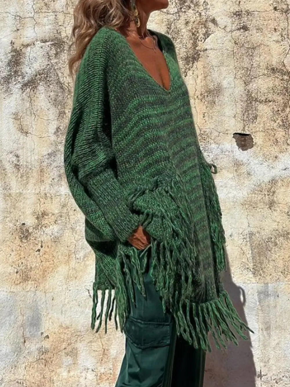 Dark green knit sweater side view with long sleeves and layered fringe at the hem.