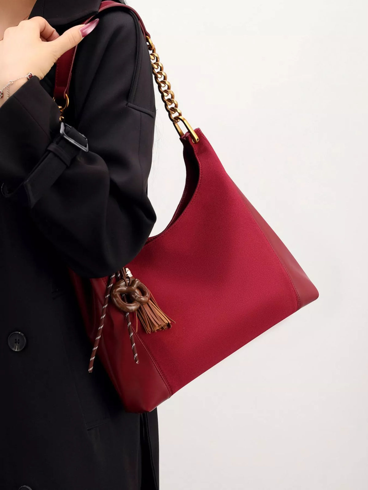 Wine red suede shoulder bag with gold chain strap and tassel, angled close-up.