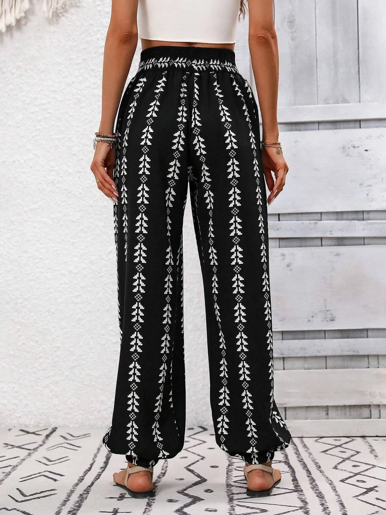 Wide-leg printed pants, black with repeating white leaf-like columns and elastic waistband