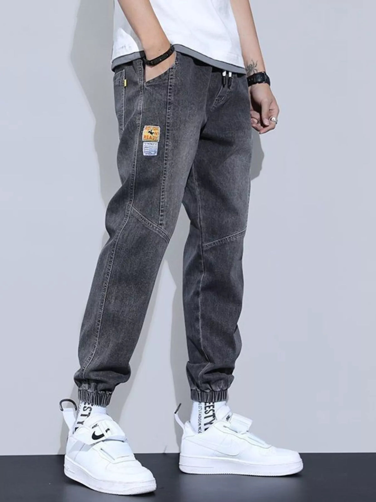 Men's washed dark gray drawstring jeans with pockets and cuffed jogger hems.