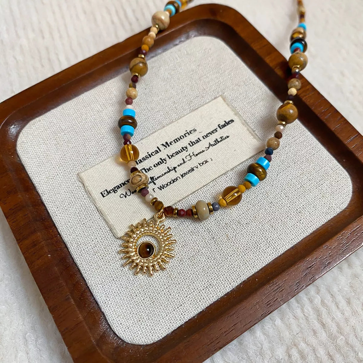Gold-tone beaded sunflower pendant necklace with multicolor beads on wooden tray