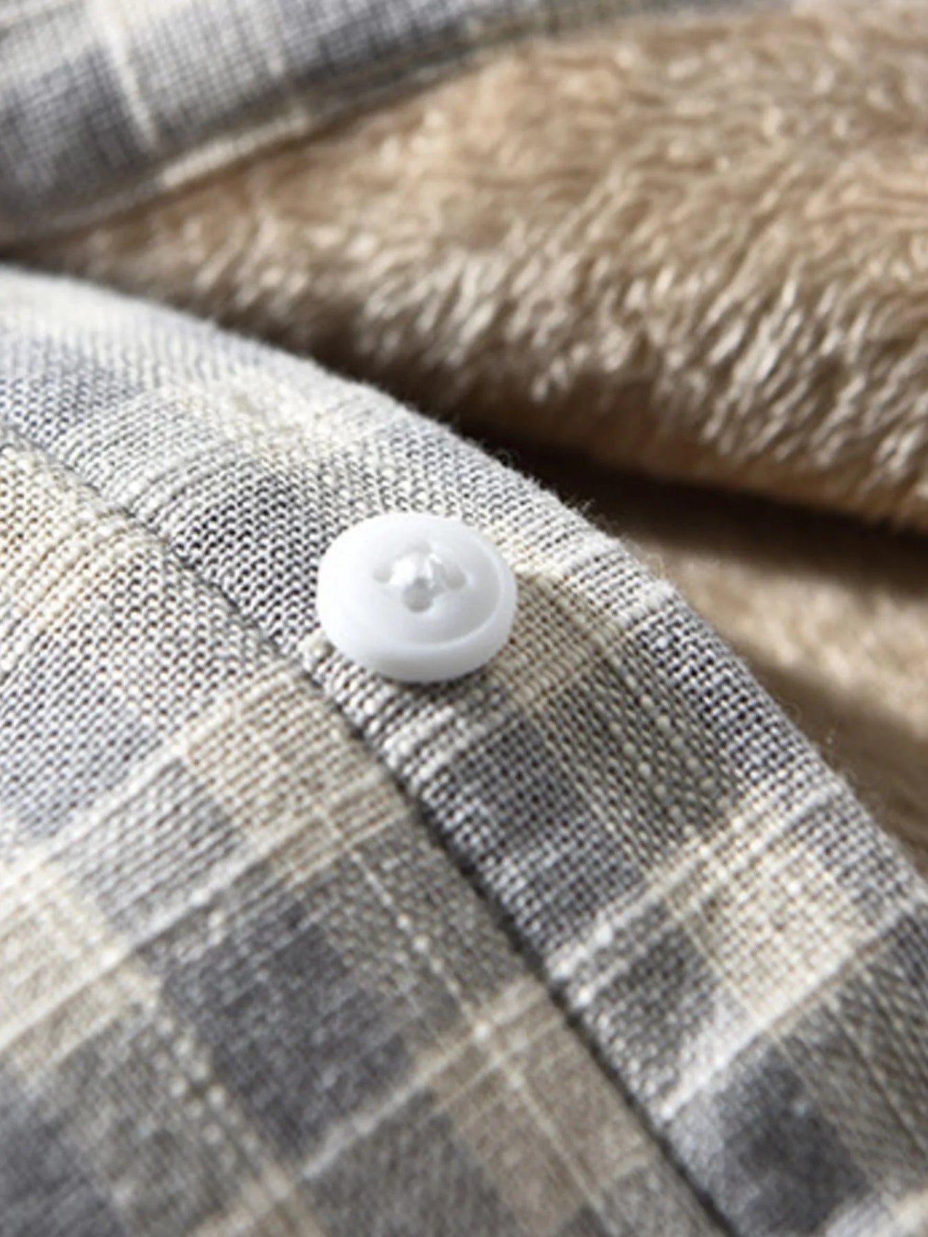 Men's plaid button-down shirt cuff with white button and light plaid fabric