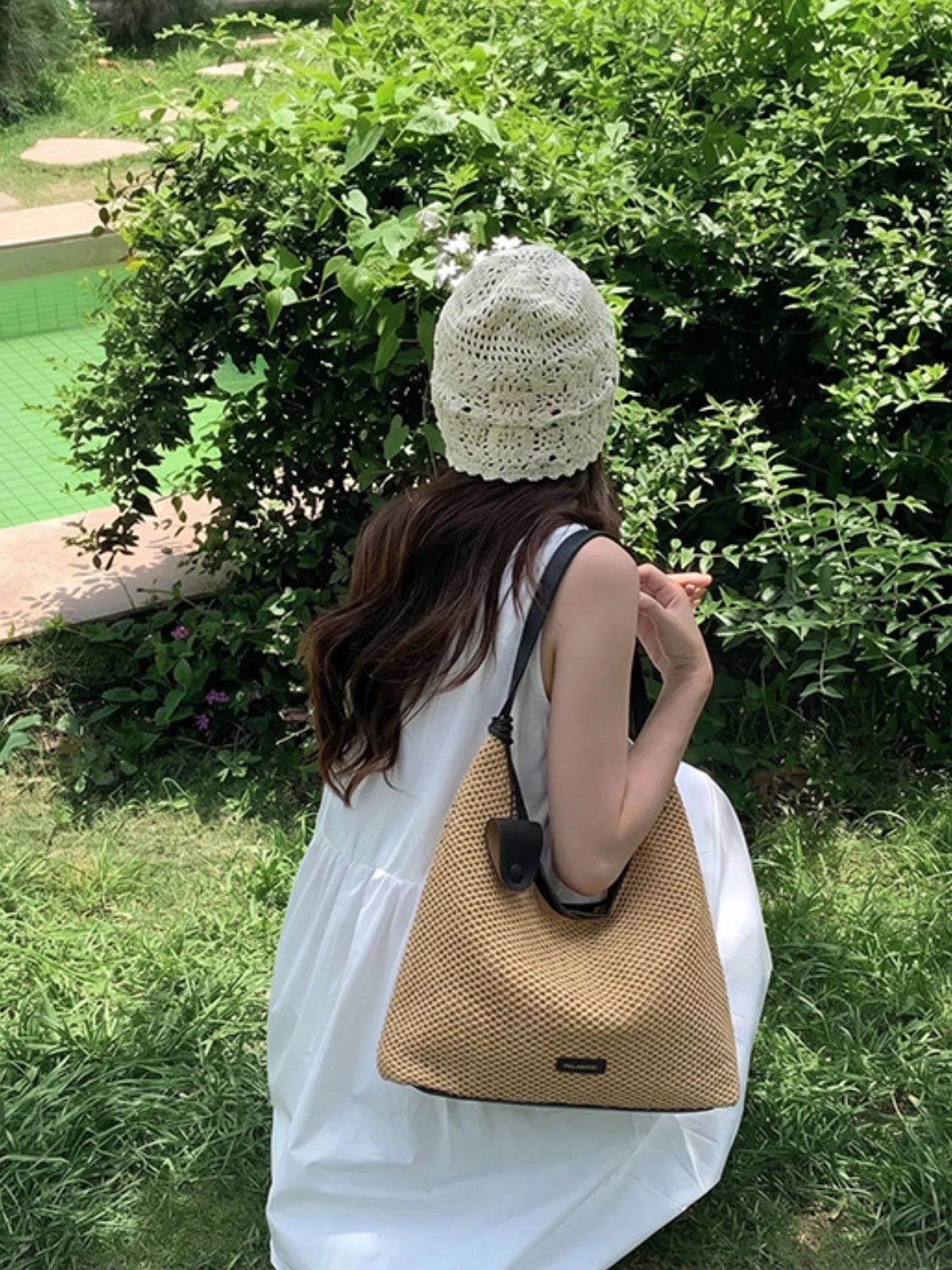 Camel woven straw shoulder bag worn over the shoulder with black handle trim