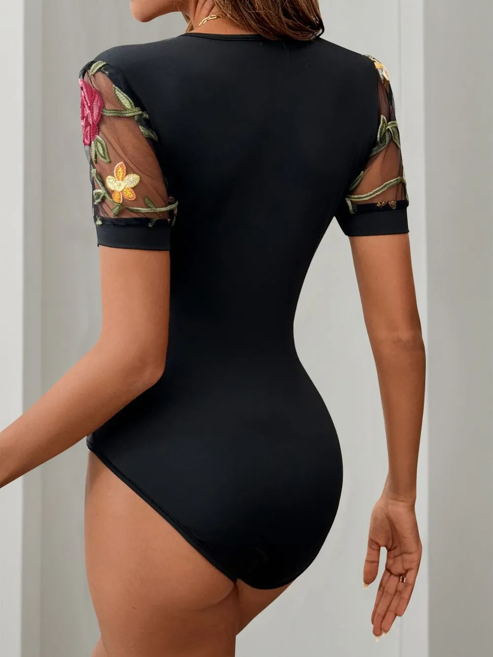 Black V-neck thong-style bodysuit with embroidered floral accents on short sleeves