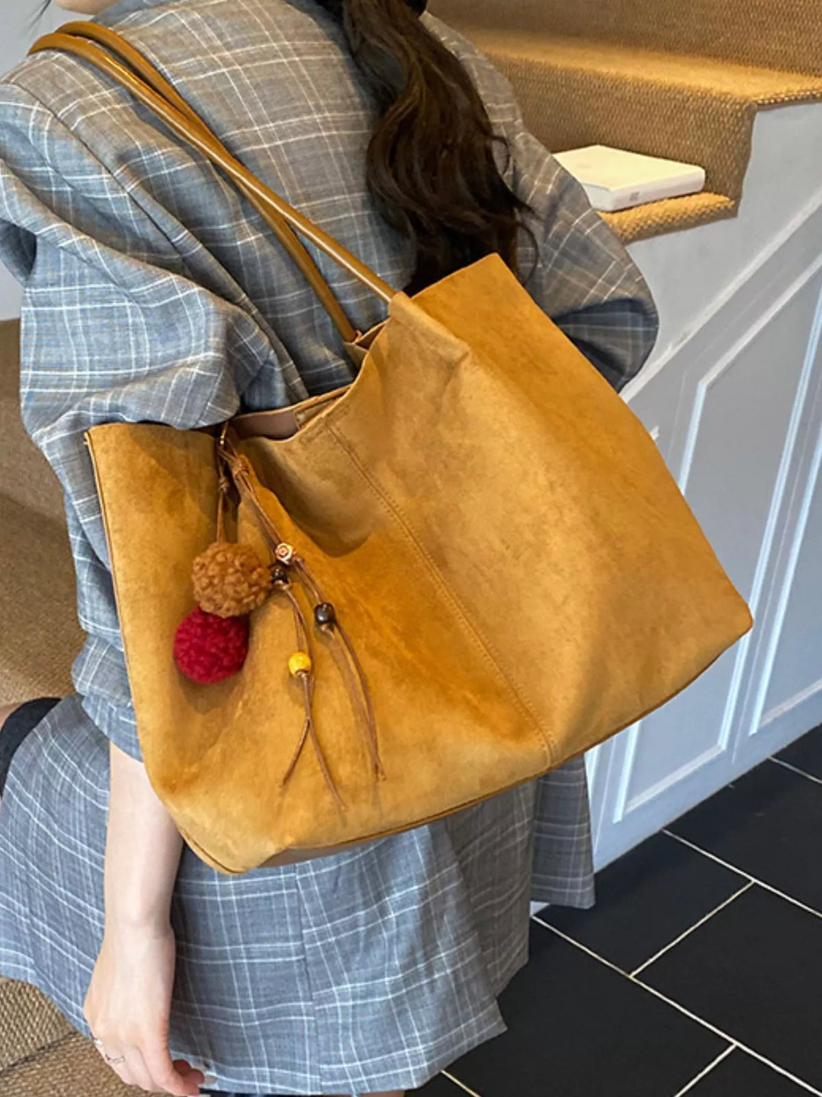 Tan suede large tote bag on shoulder; long handles and front zipper pocket with charms.