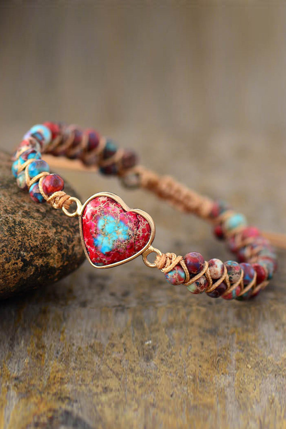 Braided bracelet with multicolor beads and gold heart-shaped stone pendant on rock