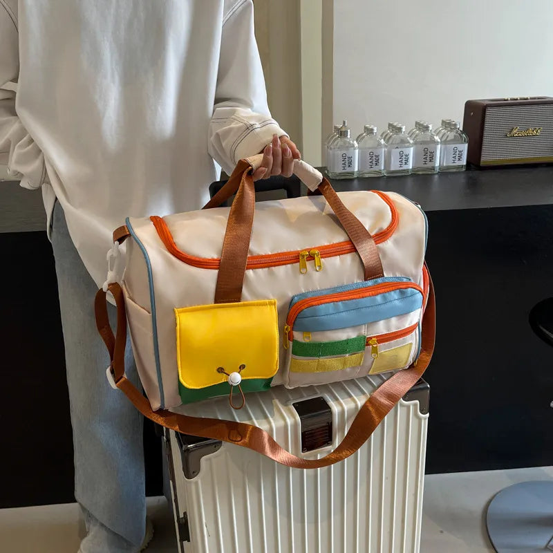 Beige travel duffle bag with orange trim, brown handles, and front flap pocket