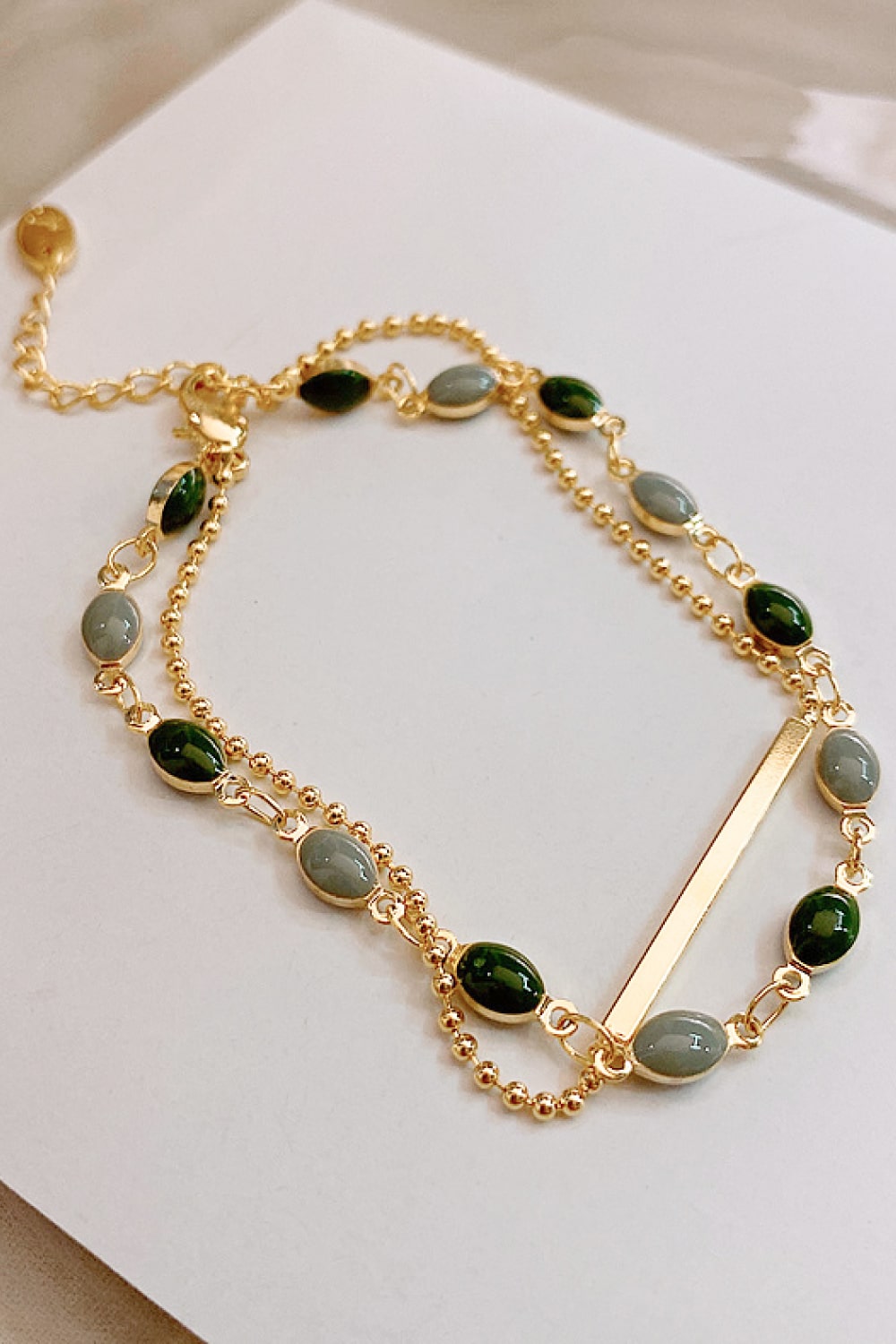 Double-layer gold-tone bracelet featuring green and gray oval beads and flat bar piece